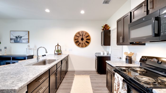 2-BR Apartments in Boerne, TX - Garden Creek - Kitchen with Granite-Style Countertops, Dark Brown Cabinets, and Black Appliances.