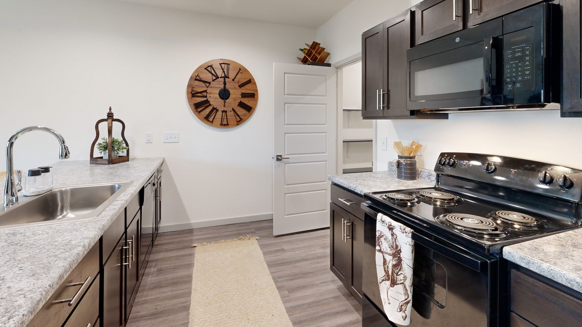 a kitchen with black cabinets and a clock on the wall at The Garden Creek Apartments